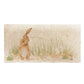 A handmade rectangle cream marble splashback tile featuring a watercolour countryside animal design of a hare in grass cleaning his ear.