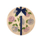 Round beech wood chopping board featuring a watercolour floral pattern of blue and pink hydrangea flowers and butterflies. The wooden board is finished with a blue gift ribbon and tag.