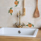 A country kitchen sink with a minimalistic splash back made up of large cream marble tiles with a single watercolour orange motif.