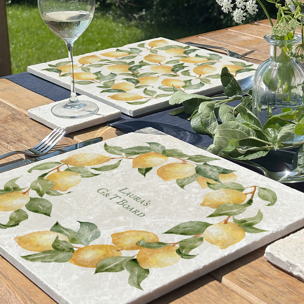 A large marble placemat personalised with the bespoke message 'Laura's G&T board'. The placemat is set on a table in a sunny garden.