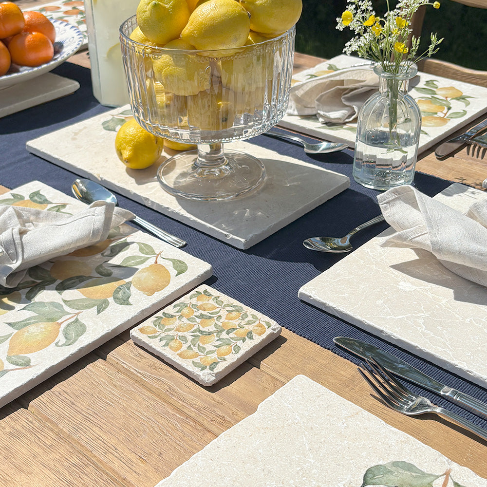 A table in a sunny garden set with marble placemats and coasters featuring a maximalist lemon pattern.