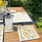 A garden table in the sunshine set with marble placemats, coasters and platters, all featuring a watercolour lemon design.