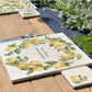 A personalised marble placemat with a lemon and leaves wreath design, with a custom personalised message in the centre. The placemat is set on a garden table in the sunshine.