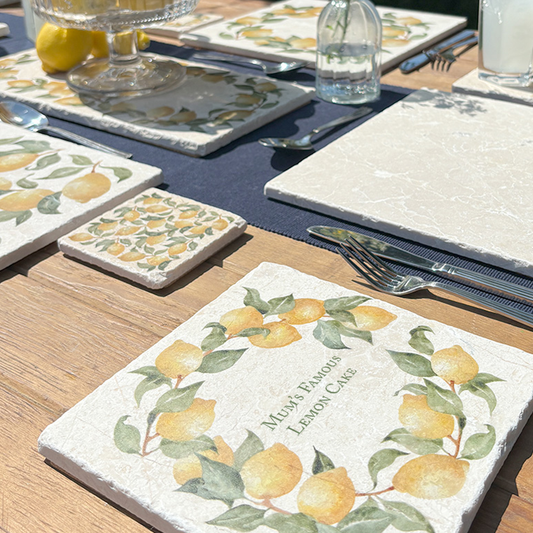 A medium marble serving board personalised with the bespoke message 'Mum’s Famous Lemon Cake’. The serving board is set on a table in a sunny garden.