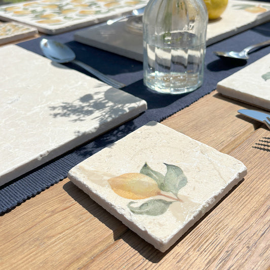 An al fresco dining table set with marble placemats and coasters featuring a minimalistic watercolour lemon design.