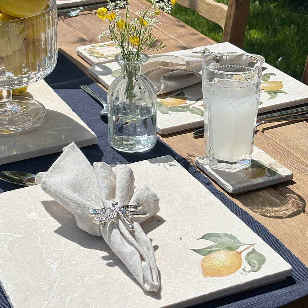 An al fresco dining table set with marble placemats and coasters featuring a minimalistic watercolour lemon design.