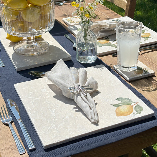 A garden table set for dining al fresco with marble placemats and coasters featuring a minimalistic watercolour lemon design.