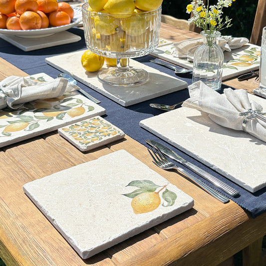 A garden table set with marble placemats and coasters that feature a watercolour lemon design.