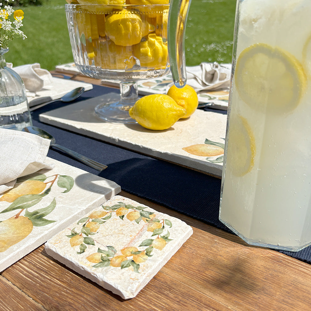 An al fresco dining table set with marble coasters and placemats featuring a watercolour lemon wreath design.