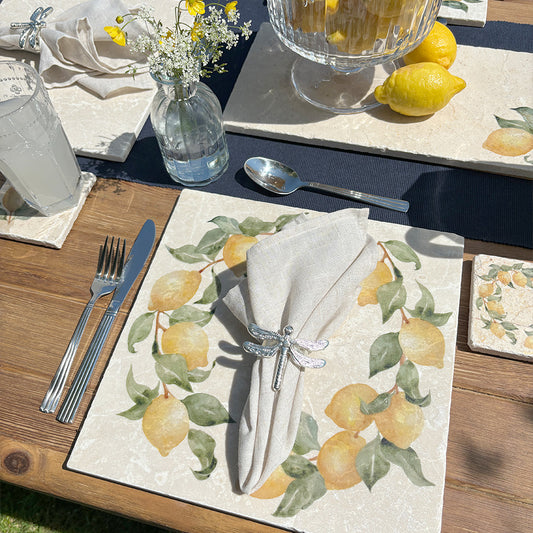 A garden table in the sunshine, the table is set with marble placemats and coasters featuring a rustic lemon wreath design.