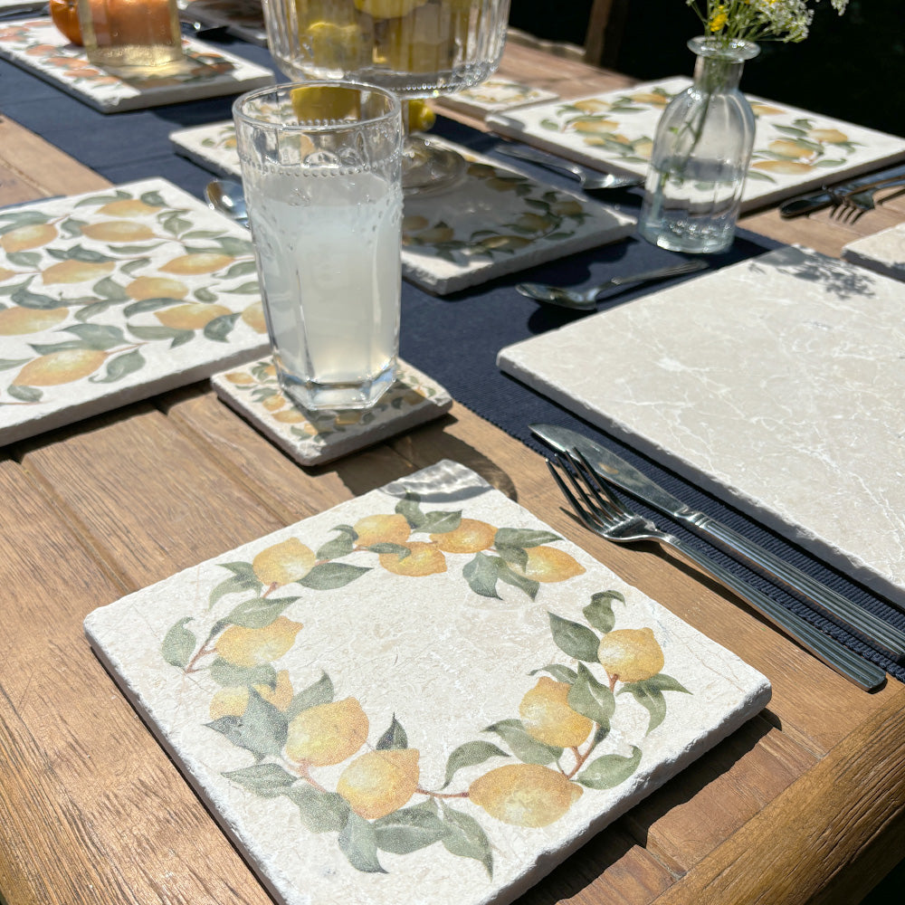 A medium square marble platter featuring a watercolour lemon wreath design. The platter is set with other marble serving platters on a garden table.