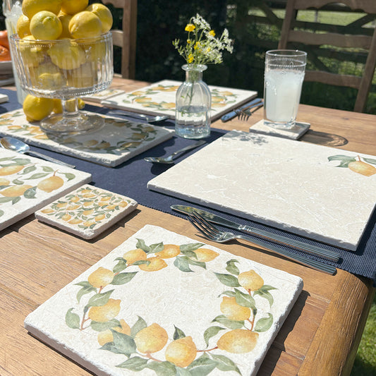 A medium square marble platter featuring a watercolour lemon wreath design. The platter is set with other marble serving platters on a garden table.