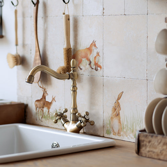 A tiled splashback behind a sink in a country farmhouse kitchen. The splashback is made up of plain marble tiles, alternated with marble tiles featuring countryside animals including hares and foxes.