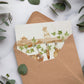 A greetings card with a watercolour scene of dormice in a garden shed. The card is inside a brown kraft envelope.