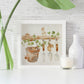 A framed greetings card with a watercolour scene of dormice in the garden shed. 