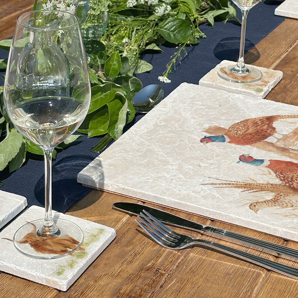 A beautiful dining table set for a dinner party with marble placemats and coasters. The coasters and placemats have mix and match designs featuring different countryside animals.