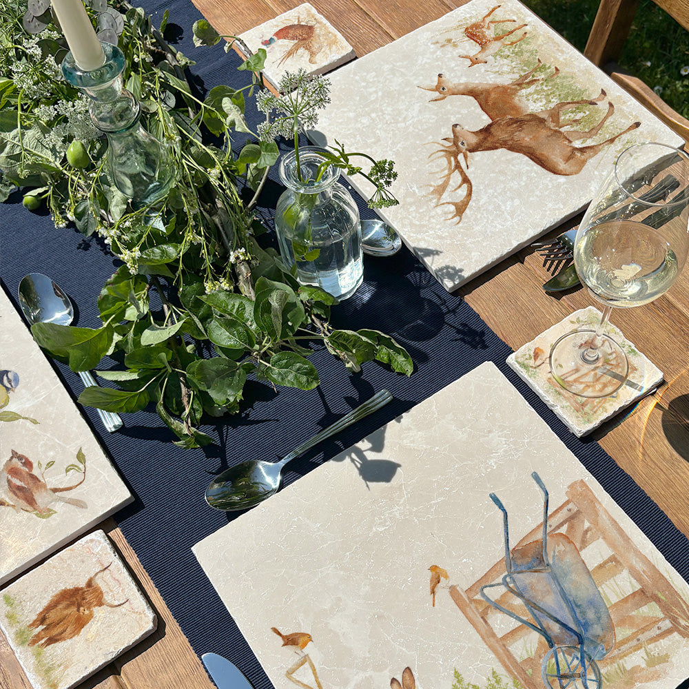 A beautiful dining table set for a dinner party with marble placemats and coasters. The coasters and placemats have mix and match designs featuring different countryside animals.