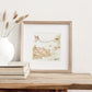 A greetings card displayed as an art print in a neutral coloured frame propped up on a bookshelf. The card reads New Home on bunting held by a sparrow and a robin above an open garden gate in a watercolour style.