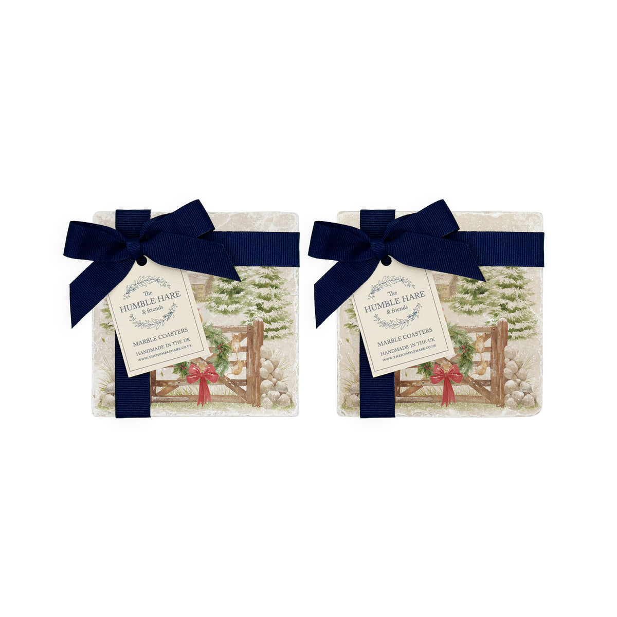 Set of four square coasters featuring a rustic Christmas scene with mice playing on a wooden gate, green wreath, red bow, snowy pine trees, and a small cottage. The coasters are tied with dark blue ribbons and bows.