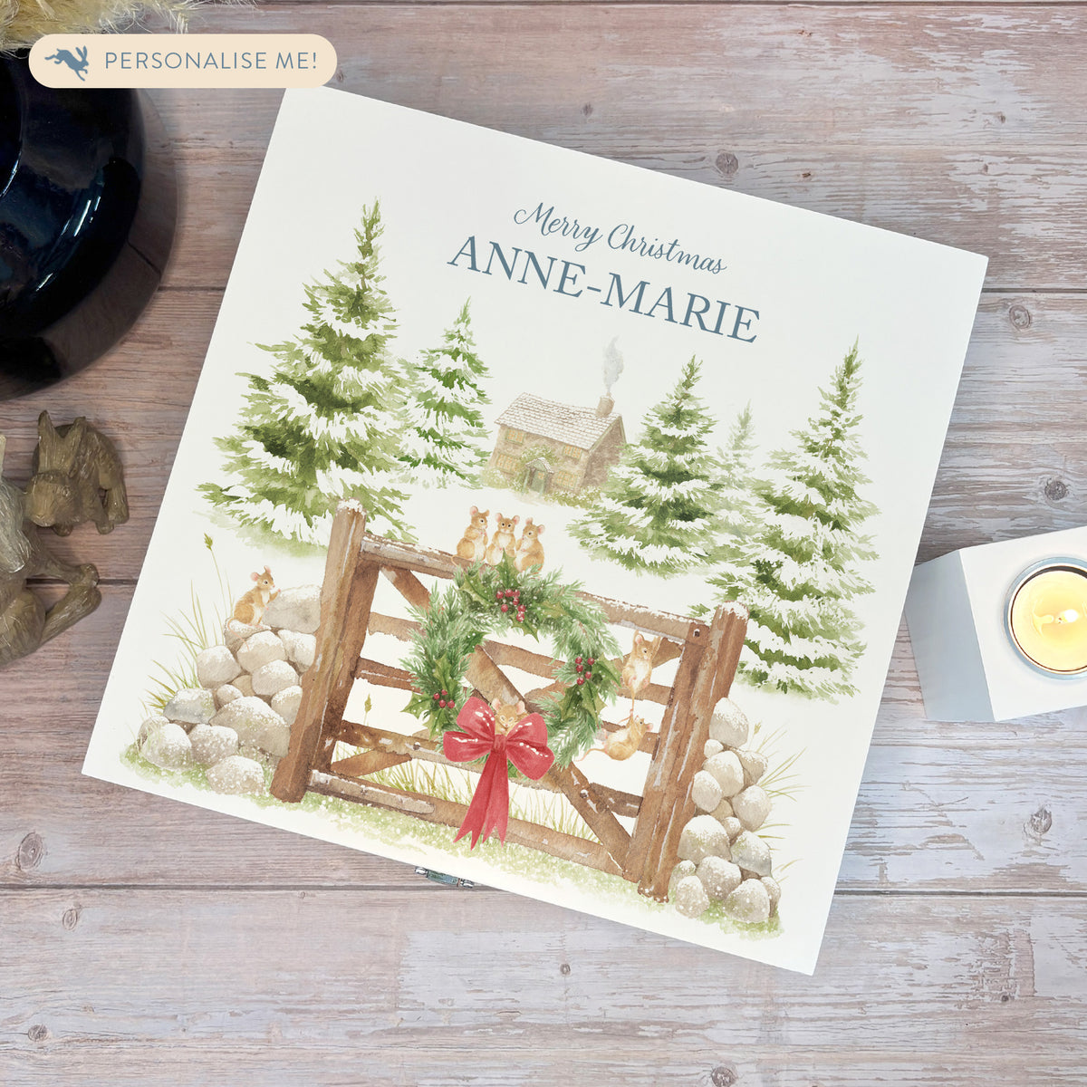 A white wooden Christmas Eve gift box with a winter scene of mice playing on a cottage gate in a snowy forest watercolour illustration, the box is personalised with a name and Merry Christmas phrase.