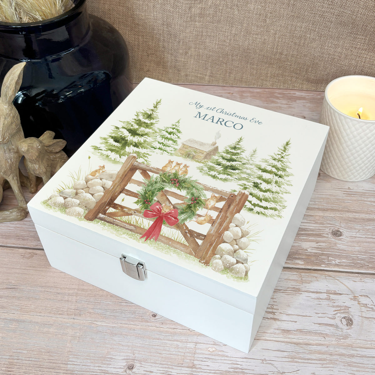 A white wooden Christmas Eve gift box with a winter scene of mice playing on a cottage gate in a snowy forest watercolour illustration, the box is personalised with a name and Merry Christmas phrase.