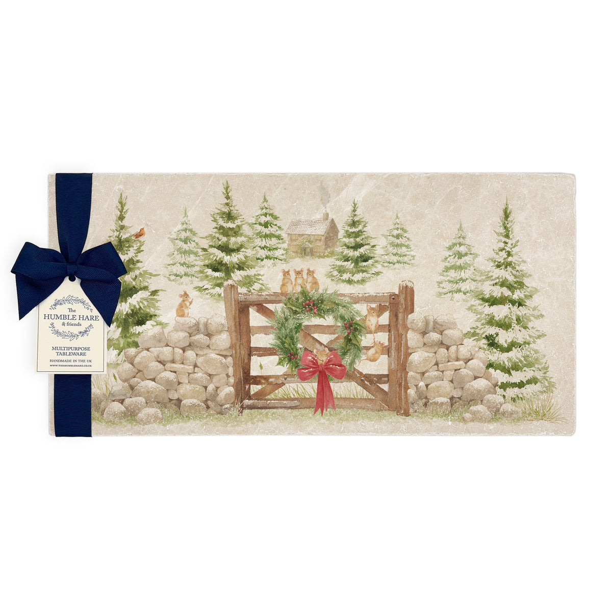 A rectangular marble sharing platter featuring a rustic winter forest scene with mice playing on a wooden gate, green wreath, red bow, stone wall, evergreen trees, and a small cabin. The platter is finished with a navy blue gift bow and paper tag,