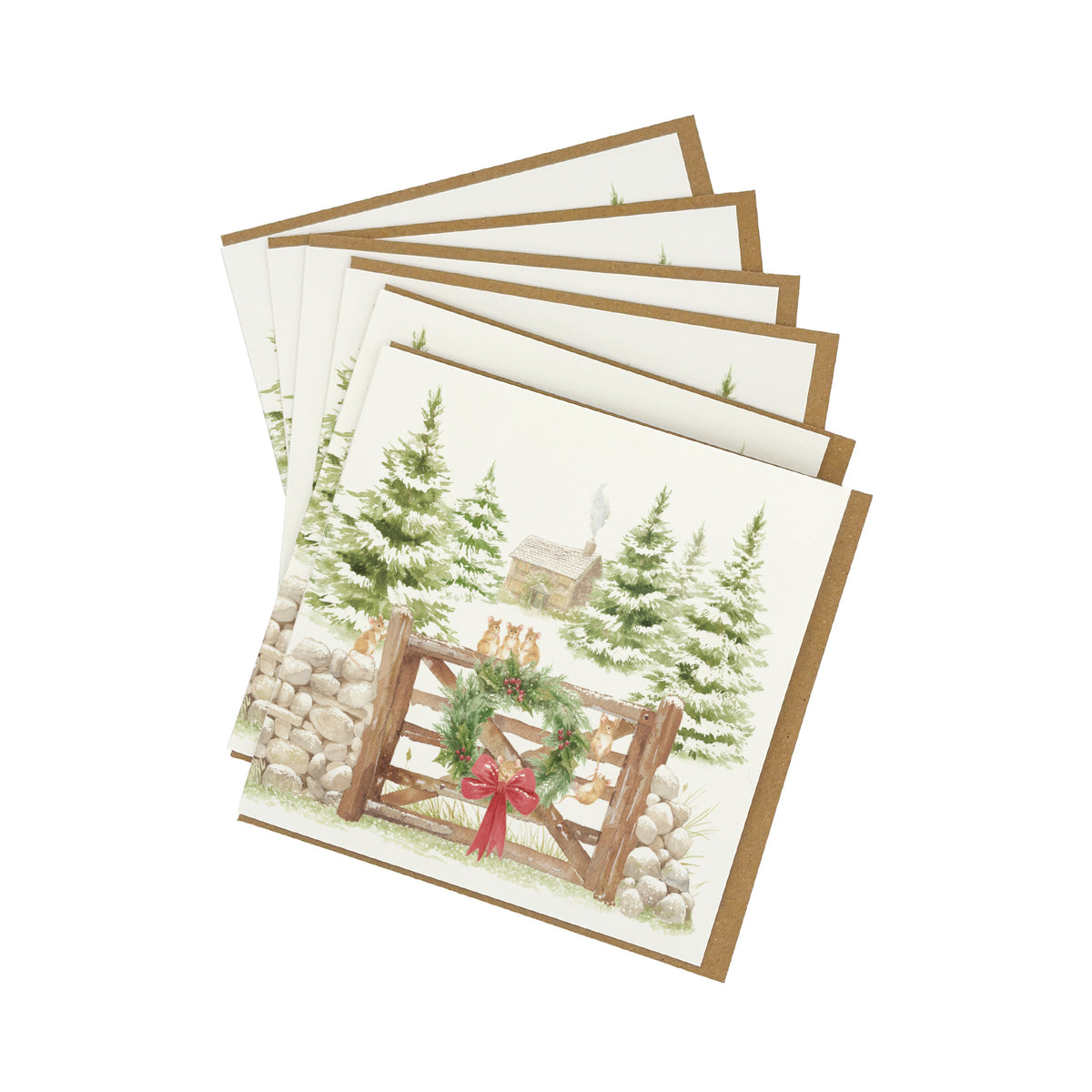 A set of 6 square greeting cards fanned out on a white background, each with a brown envelope. The front card features a winter landscape illustration with snow-covered evergreen trees, a rustic cabin, and a wooden fence decorated with a green wreath and red bow.