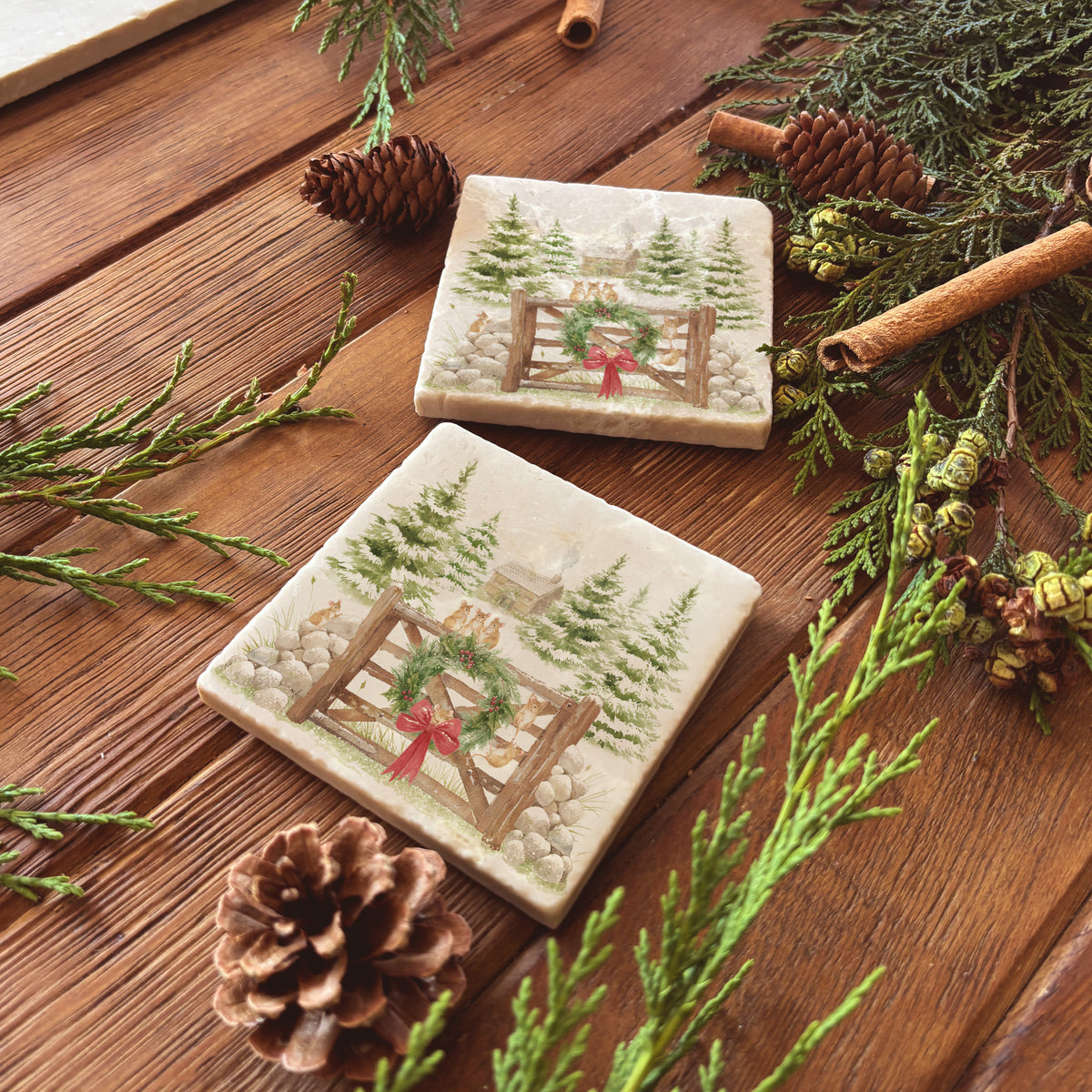 Set of four square coasters featuring a rustic Christmas scene with mice playing on a wooden gate, green wreath, red bow, snowy pine trees, and a small cottage.
