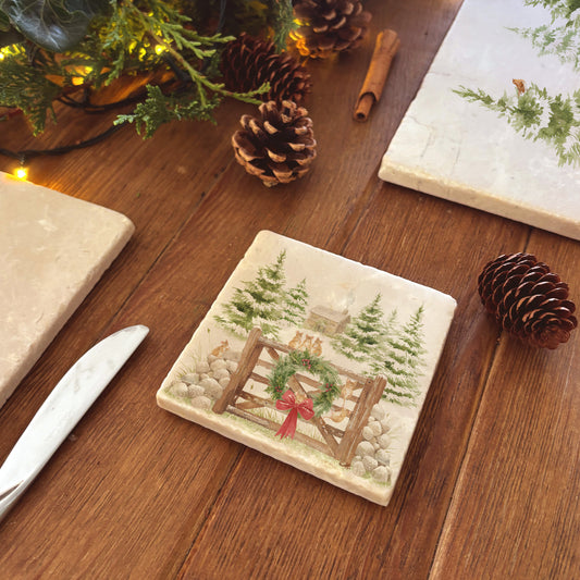Set of four square coasters featuring a rustic Christmas scene with mice playing on a wooden gate, green wreath, red bow, snowy pine trees, and a small cottage.