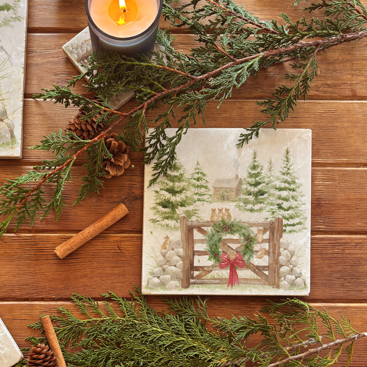 A square medium marble platter featuring a winter landscape watercolour illustration with snow-covered evergreen trees, a small cabin, mice playing on a wooden gate, a green wreath, and a red bow, 