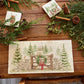 A rectangular marble sharing platter featuring a rustic winter forest scene with mice playing on a wooden gate, green wreath, red bow, stone wall, evergreen trees, and a small cabin.