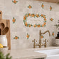 A kitchen backsplash made of beige marble tiles decorated with orange and green fruit watercolour design including a central wreath design with the text 'Our Happy Place' above a brass faucet and stone countertop.