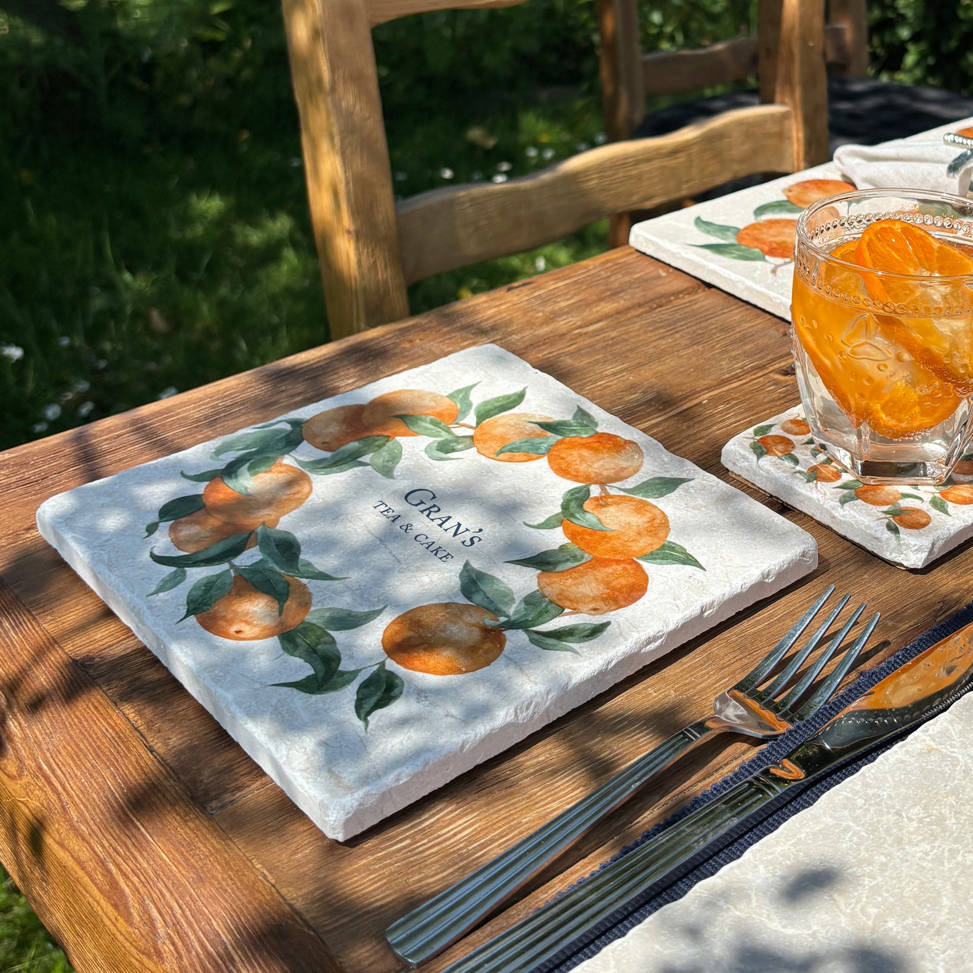 A medium personalised square marble platter featuring a watercolour orange wreath design. The platter is set next to a marble placemat and coaster to be used as a side plate.