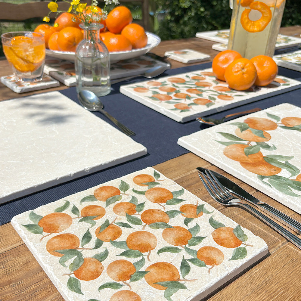 A garden table in the sunshine set with marble placemats, coasters and platters, all featuring a watercolour orange design.