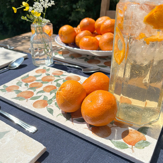 A table in the garden set with iced drinks and pretty flowers, placed on multipurpose marble platters featuring a watercolour orange pattern.