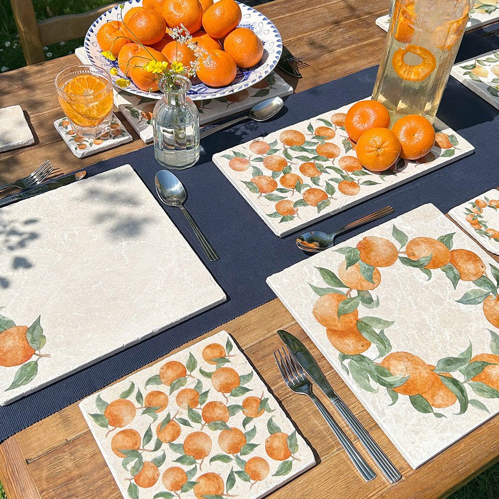 A garden table set with multipurpose marble platters ready for a dinner party. The platters feature a summery pattern of oranges and green leaves.