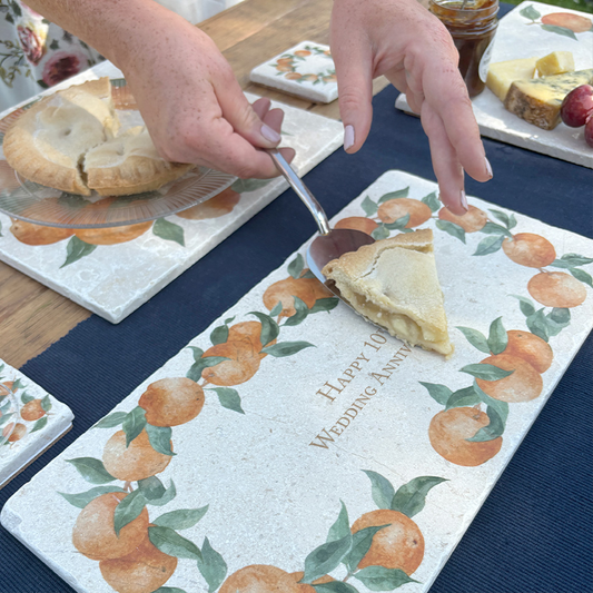 A personalised marble sharing board featuring a wreath of oranges and leaves, with a bespoke message in the centre of the design reading Happy 10th Wedding Anniversary'. The custom sharing platter is being used to serve apple pie.