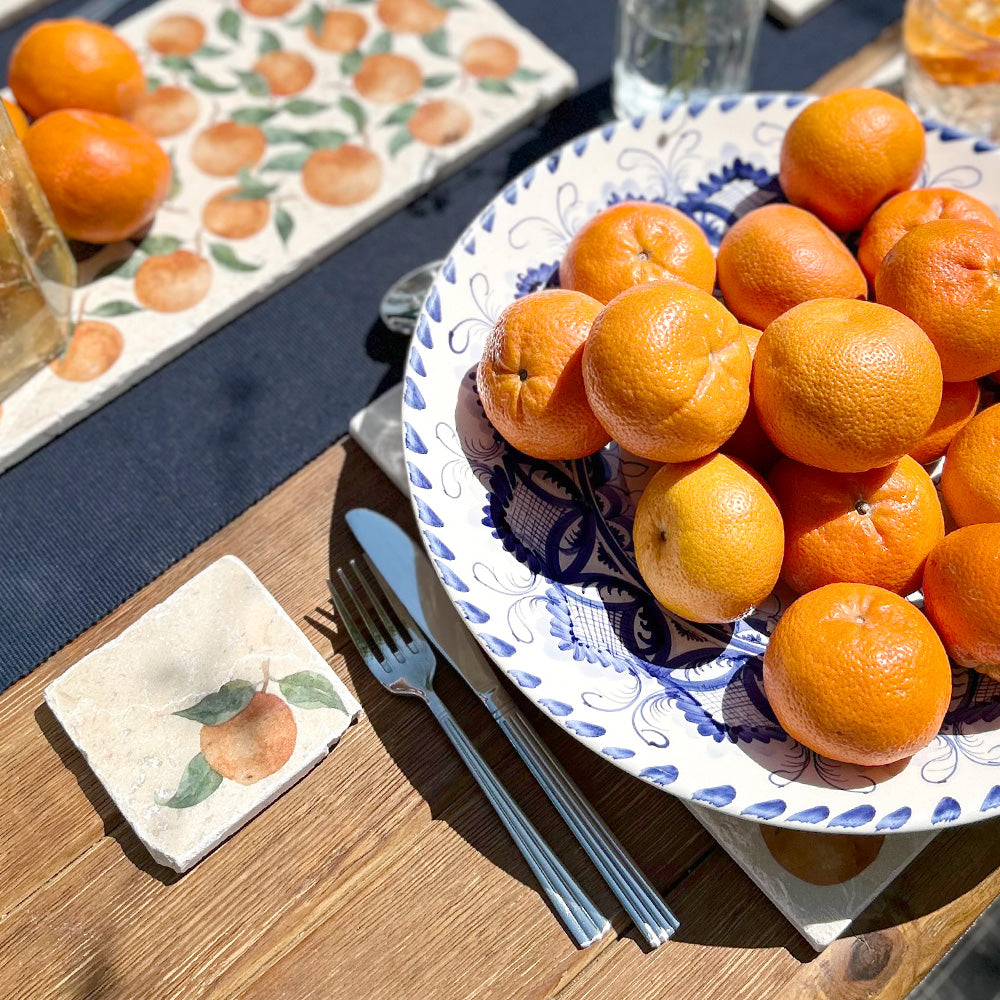 A marble coaster featuring a minimalistic watercolour orange and leaves design set on a beautiful table dressed for an al fresco dinner party.