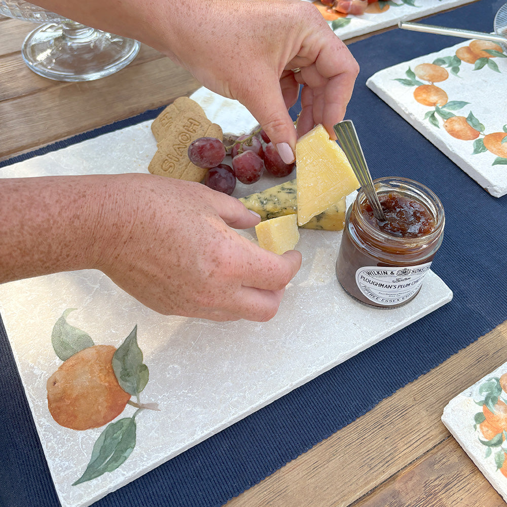 A large marble cheeseboard with a minimalistic orange design, being used to serve a selection of cheese, crackers and chutneys.