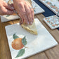 A medium marble platter featuring a simple design of a single watercolour orange with leaves. The platter is being used to serve a slice of apple pie.