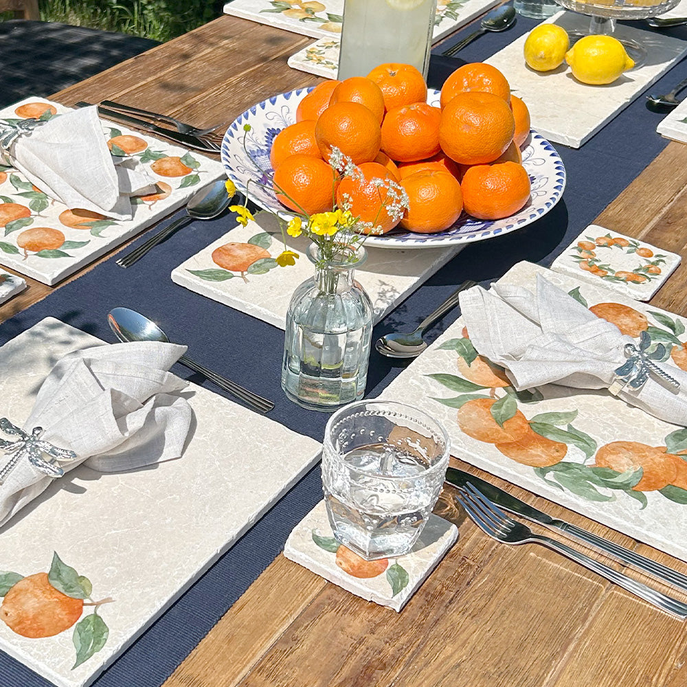 A garden table set with marble placemats and serving platters featuring a minimalistic orange watercolour design.