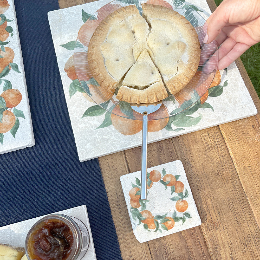 An al fresco dining table set with marble coasters and placemats featuring a watercolour orange wreath design.