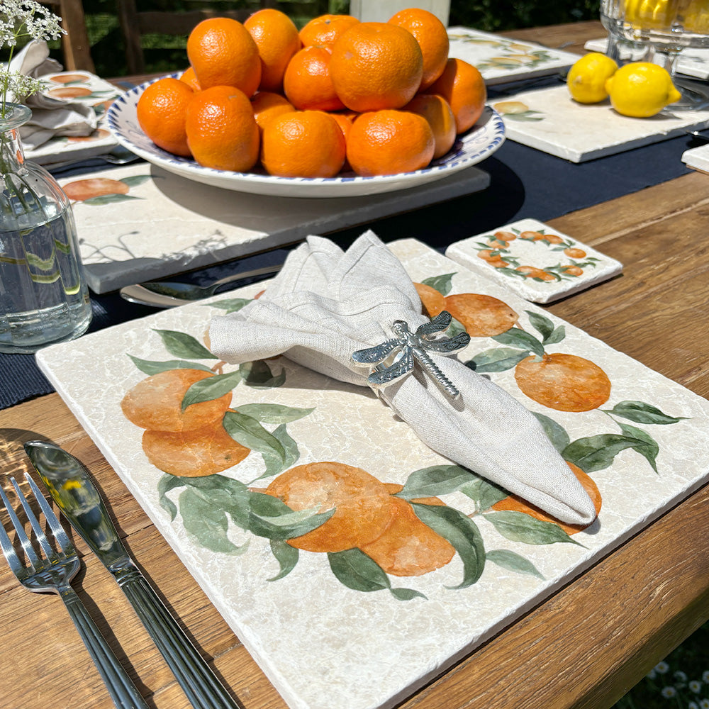 A garden table in the sunshine, the table is set with marble placemats and coasters featuring a rustic orange wreath design.