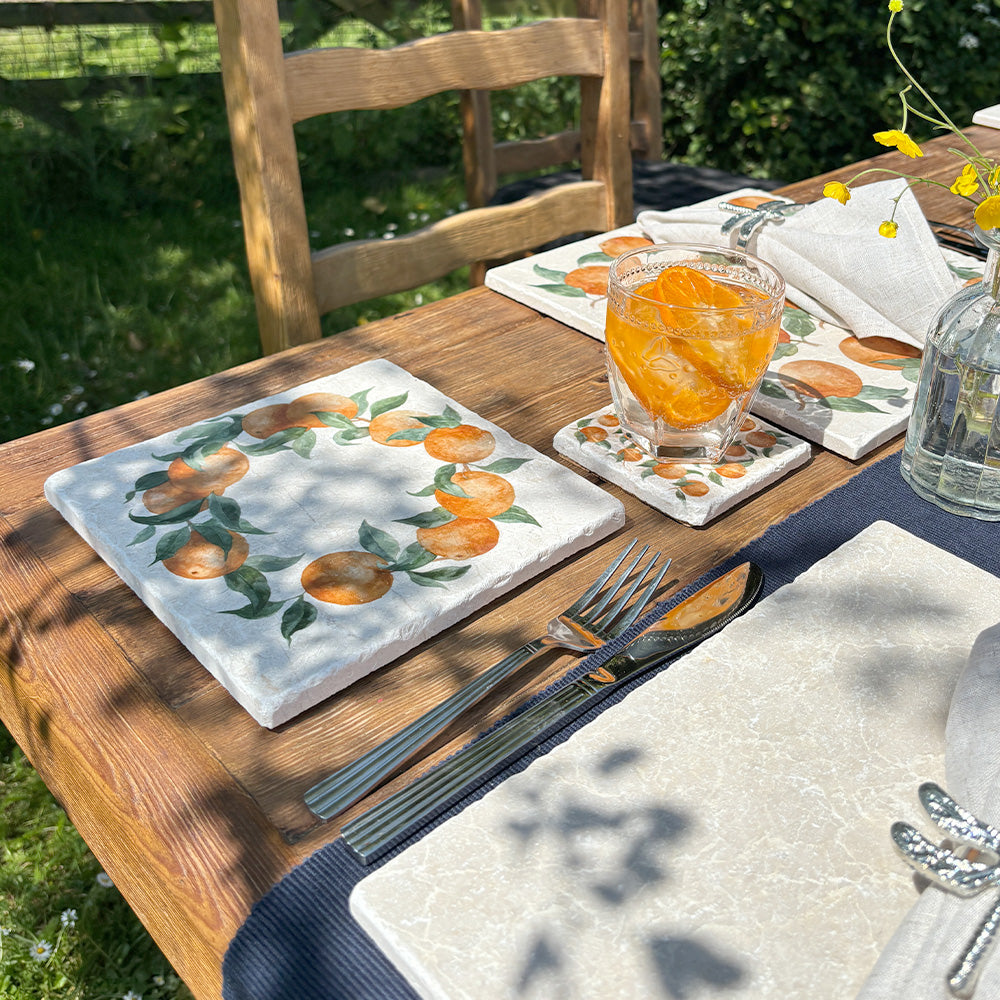 A medium square marble platter featuring a watercolour orange wreath design. The platter is set next to a marble placemat and coaster to be used as a side plate.