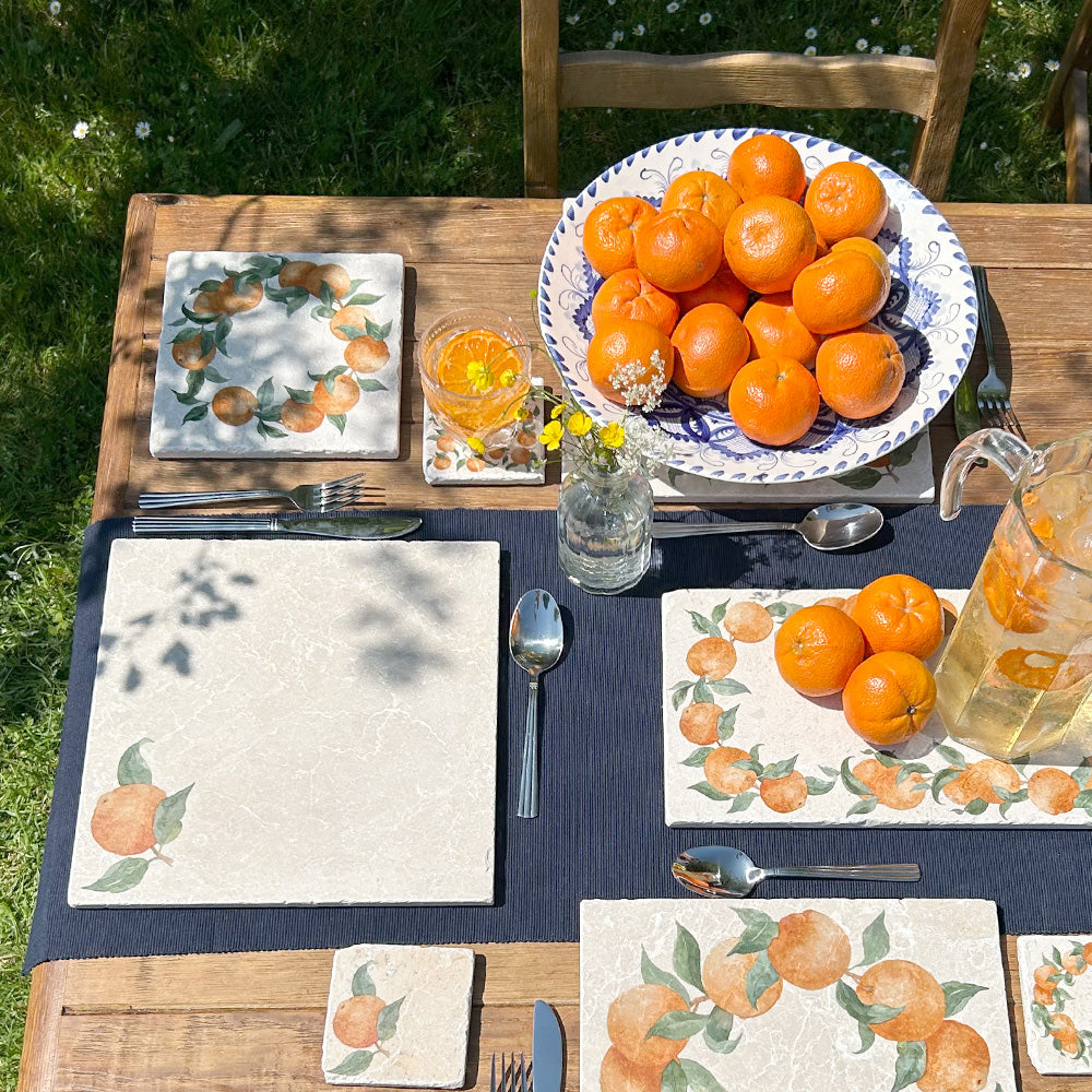 An al fresco dinner table set with a collection of marble platters and coasters, all featuring vibrant watercolour oranges and leaves.