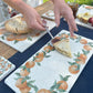 A marble sharing platter featuring a watercolour wreath of fresh oranges and green leaves. A slice of apple pie is being served onto the platter.