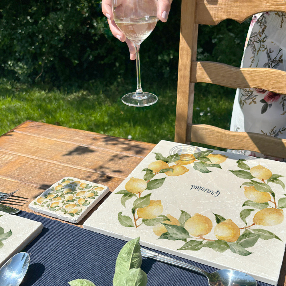 A beautiful garden table set with personalised marble placemats and coasters, ready for a dinner party. The placemats feature a lemon wreath design.