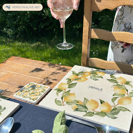 A beautiful garden table set with personalised marble placemats and coasters, ready for a dinner party. The placemats feature a lemon wreath design.