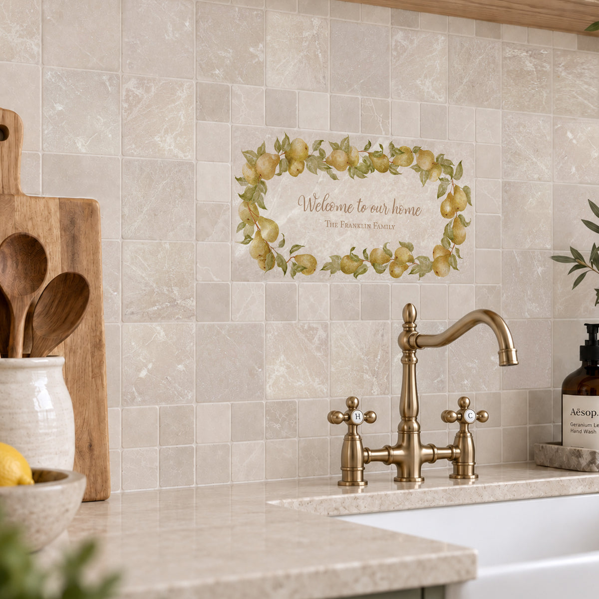 A decorative wall decal featuring a watercolor lemon wreath and the text 'Welcome to our home The Flowers Corner' is shown on a beige tiled kitchen backsplash above a sink with a brass faucet.