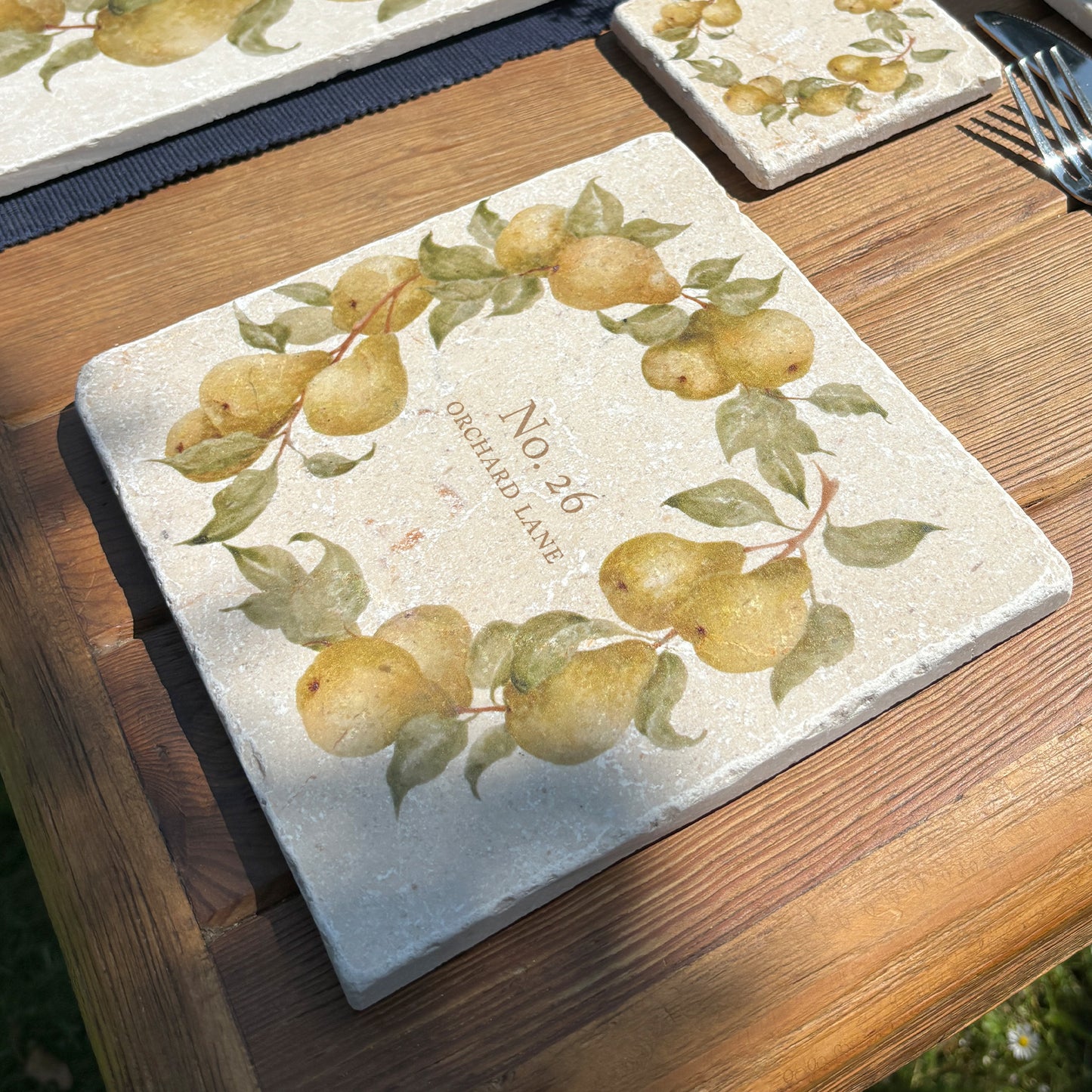 A medium personalised square marble platter featuring a watercolour pear wreath design. The platter is set on a dinner table next to a marble placemat and coaster.